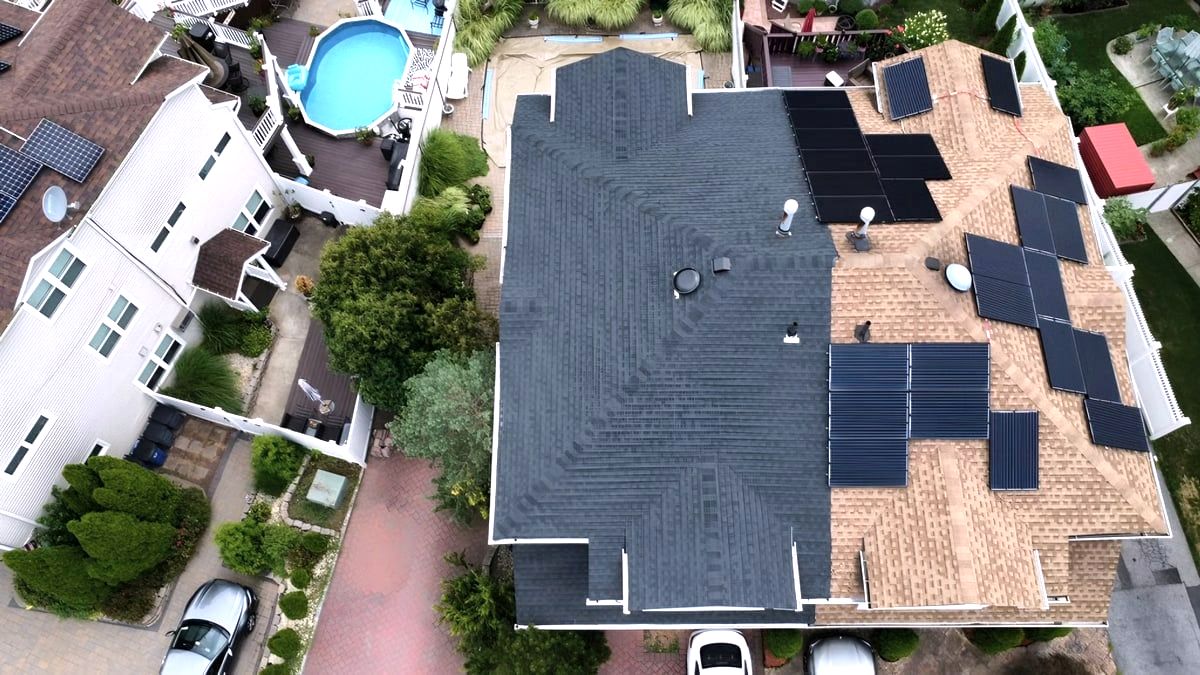 Aerial of house roof half replaced with dark shingles, solar panels